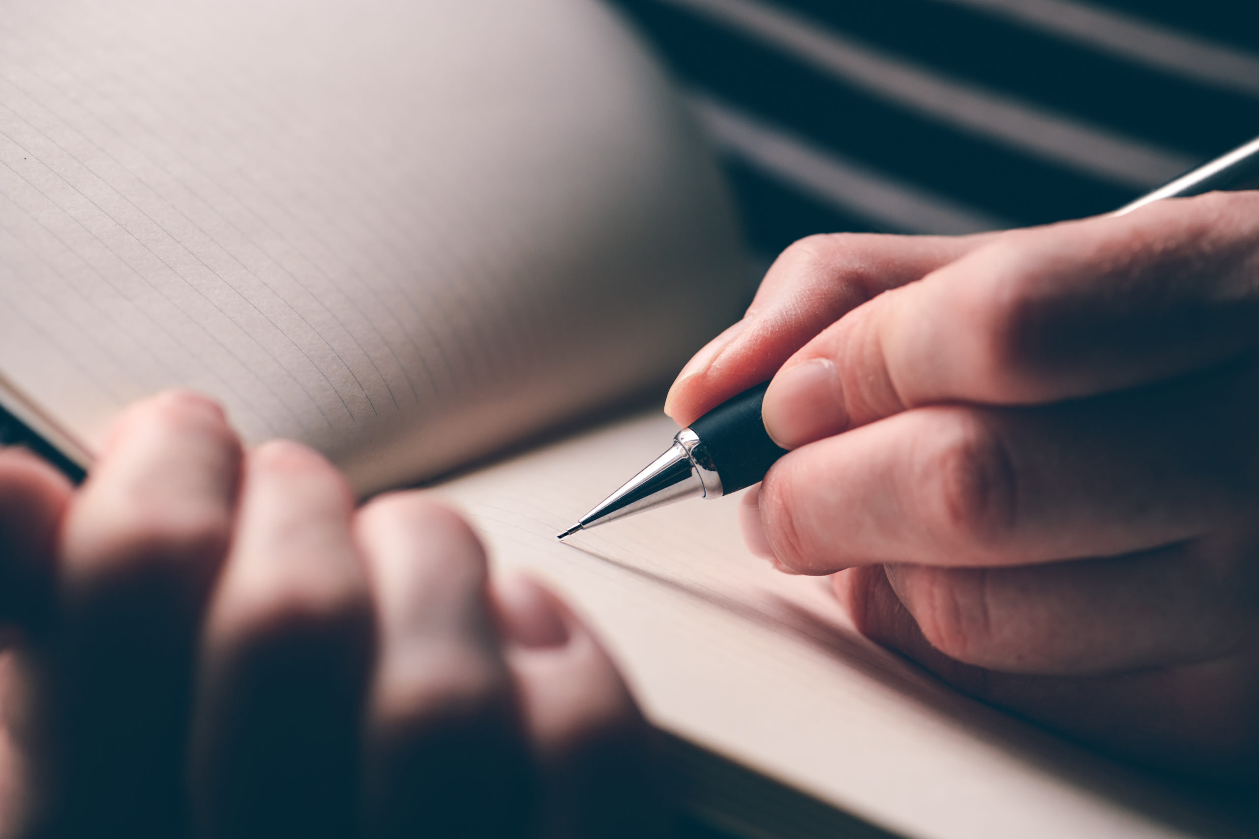 Left-handed woman writing diary, close up of hands with pencil and notebook