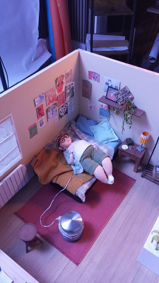 Personnage textile dans une chambre miniature.
